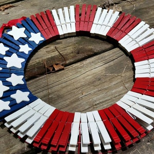 May include: A red, white, and blue patriotic wreath made from wooden clothespins. The wreath is decorated with white stars on a blue background.