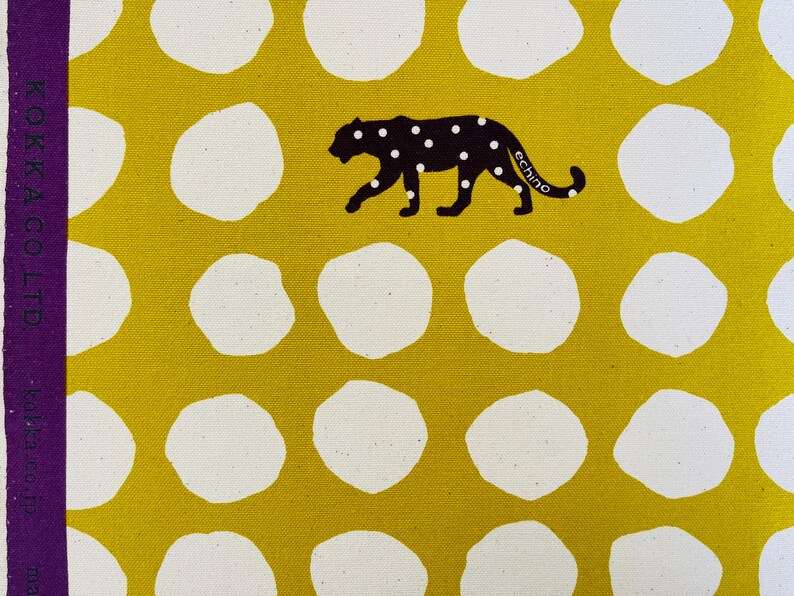 May include: Yellow fabric with white polka dots and a black silhouette of a leopard with the word "echino" printed on it. The fabric has the words "KOKKA CO LTD" printed on the side.