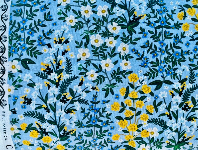 May include: A blue fabric with a floral pattern featuring white, yellow, and blue flowers. The fabric has a light blue background with a repeating pattern of flowers and leaves.