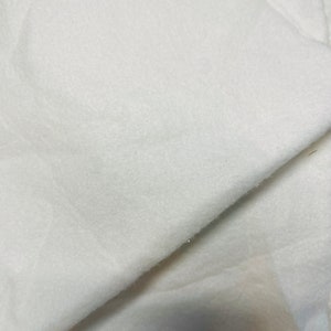 May include: White fleece fabric, soft and fluffy, with a smooth texture. The fabric is folded in half, showing the inside and outside of the material.