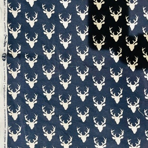 Peut inclure: Un tissu bleu marine avec un motif répétitif blanc de silhouettes de cerfs. Le tissu a du texte sur le côté qui dit "Feel the Difference | artgalleryfabrics.com 99% Cotton-5% Spandex #WE fabrics #HelloBear fabrics"
