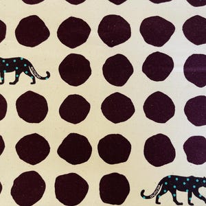 May include: A white fabric with a repeating pattern of dark purple circles and black leopards with turquoise spots. The leopards are walking to the right.