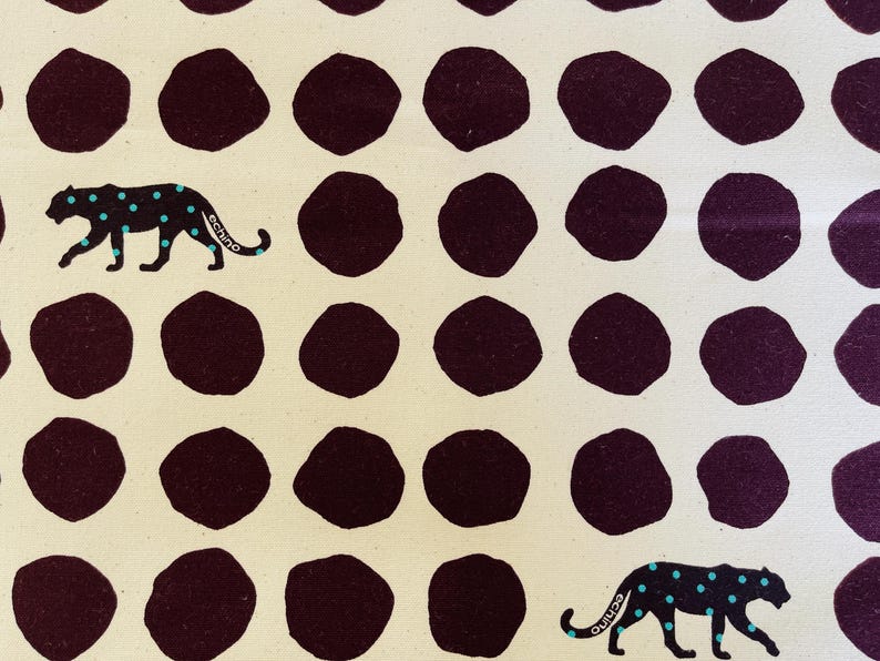 May include: A white fabric with a repeating pattern of dark purple circles and black leopards with turquoise spots. The leopards are walking to the right.