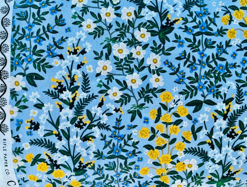 May include: A blue fabric with a floral pattern featuring white, yellow, and blue flowers. The fabric has a light blue background with a repeating pattern of flowers and leaves.