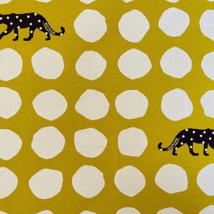 May include: A yellow fabric with a white polka dot pattern and two black silhouettes of leopards with white spots. The leopards are walking in opposite directions.