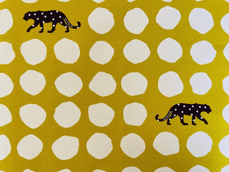 May include: A yellow fabric with a white polka dot pattern and two black silhouettes of leopards with white spots. The leopards are walking in opposite directions.