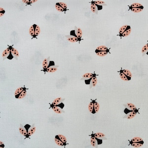 May include: White fabric featuring a repeating pattern of pink and black ladybirds. The ladybirds are scattered across the surface, some with wings open, others closed. The fabric has a slightly textured appearance.