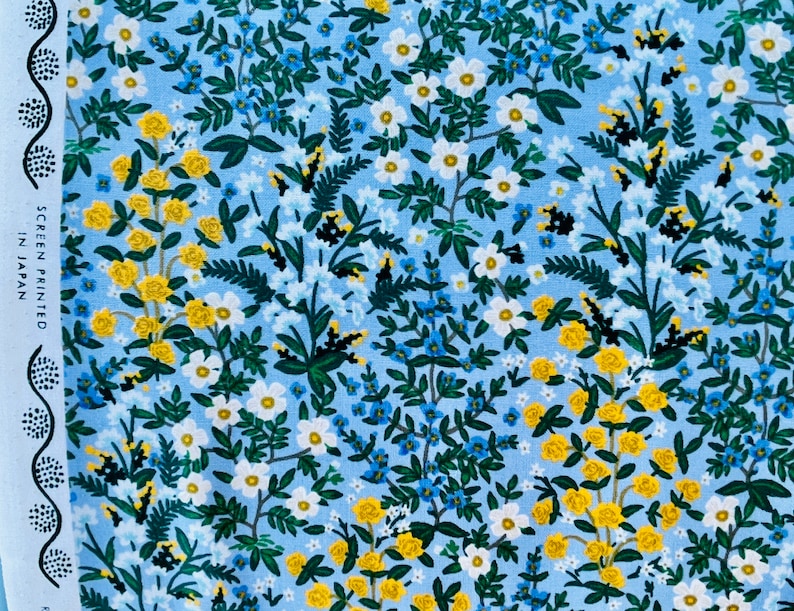 May include: A blue fabric with a floral pattern. The pattern features small white flowers, yellow flowers, and green leaves. The fabric has the text "SCREEN PRINTED IN JAPAN" on the left side.