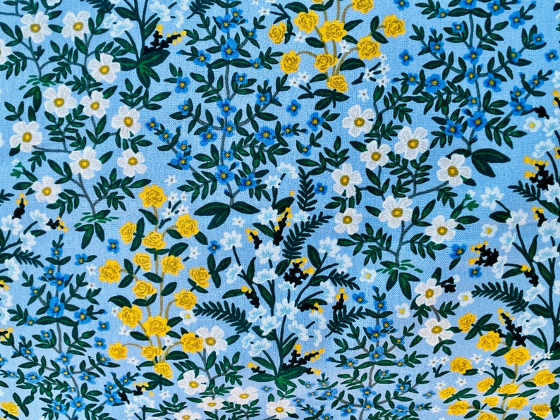 May include: A blue fabric with a floral pattern featuring white, yellow, and blue flowers. The fabric has a repeating pattern of small flowers and leaves.