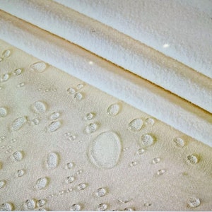 May include: Close-up of a white fabric with water droplets on the surface. The fabric is soft and appears to be waterproof.