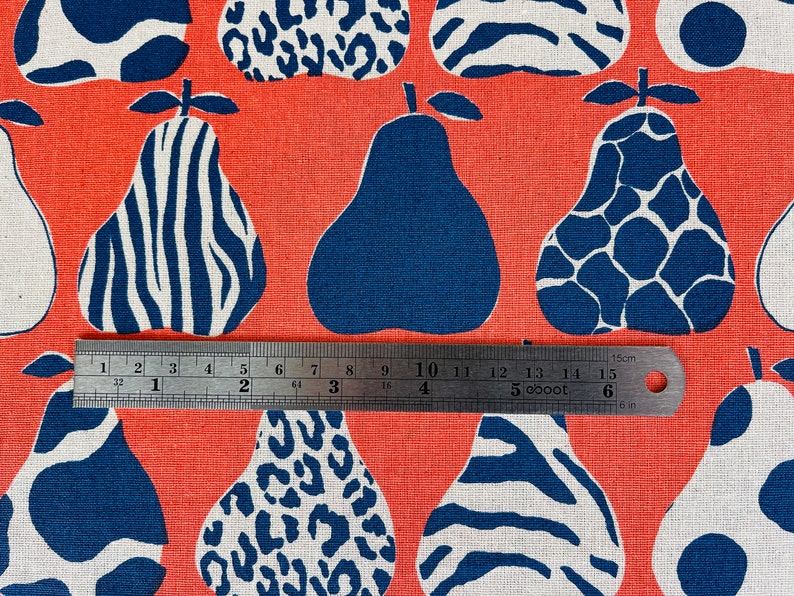 May include: A coral orange fabric with a repeating pattern of blue and white pears. The pears have different patterns, including zebra stripes, leopard spots, and a giraffe-like pattern. A ruler is placed across the fabric, measuring 15 cm.