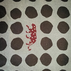 May include: A gray fabric with a repeating pattern of black circles. A red and white spotted animal is in the center of the fabric.
