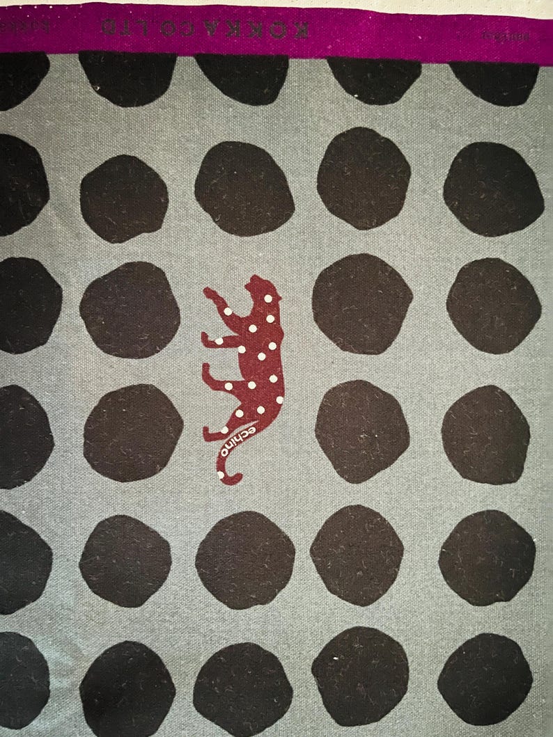May include: A gray fabric with a repeating pattern of black circles. A red and white spotted animal is in the center of the fabric.