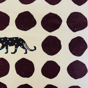 May include: A white fabric with a repeating pattern of dark purple circles. A black panther with turquoise spots walks across the fabric. The panther has the word "echino" written on its side.