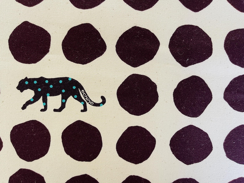 May include: A white fabric with a repeating pattern of dark purple circles. A black panther with turquoise spots walks across the fabric. The panther has the word "echino" written on its side.