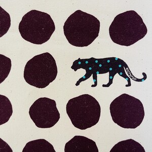 May include: White fabric with a repeating pattern of dark purple circles and a black panther with turquoise spots. The panther is walking to the right and has the word "echino" printed on its tail.