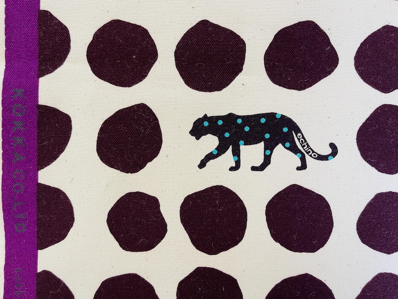 May include: White fabric with a repeating pattern of dark purple circles and a black panther with turquoise spots. The panther is walking to the right and has the word "echino" printed on its tail.