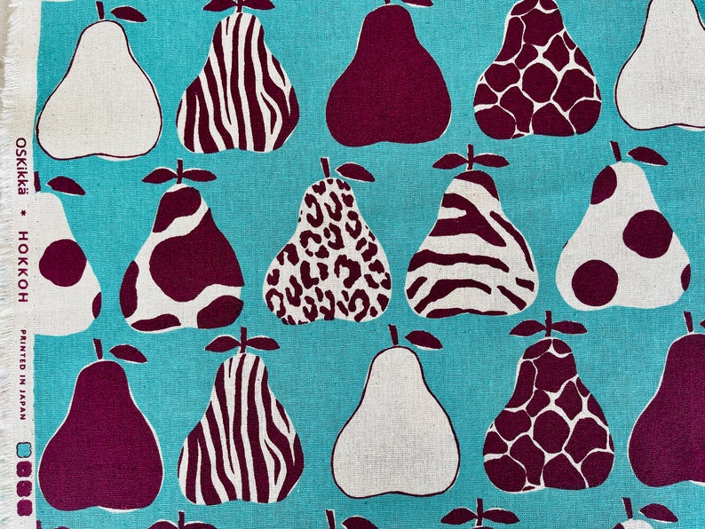 May include: A turquoise fabric with a repeating pattern of pears. The pears are in various shades of white, brown, and burgundy. Each pear has a different pattern, including zebra stripes, leopard spots, and polka dots. The fabric has the text "OSKIKKA - HOKKOH PRINTED IN JAPAN" in the bottom left corner.