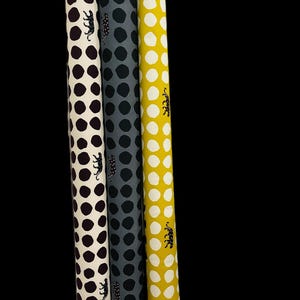 May include: Three rolls of fabric with white backgrounds and different colored polka dots. The fabric rolls are purple, gray, and yellow with black leopard print designs.