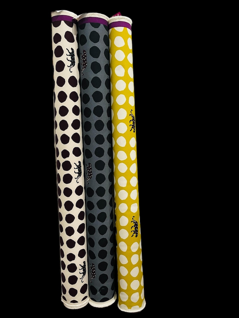 May include: Three rolls of fabric with white backgrounds and different colored polka dots. The fabric rolls are purple, gray, and yellow with black leopard print designs.