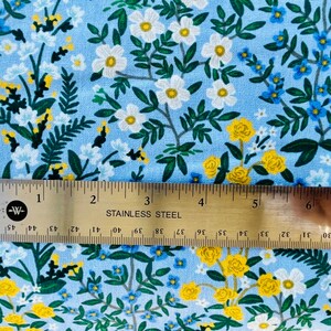 May include: A blue fabric with a white and yellow floral pattern. The fabric is measured with a ruler that reads "STAINLESS STEEL".