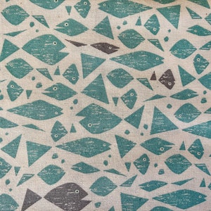 Puede incluir: Una tela beige con un patrón repetitivo de peces azul turquesa y formas geométricas. Los peces son estilizados y tienen un aspecto texturizado.