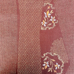 May include: A brown fabric with a repeating pattern of small white dots and a floral design. The floral design features white flowers with yellow centers and brown stems.