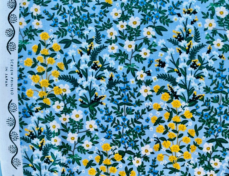 May include: A blue fabric with a floral pattern. The pattern features small white flowers, yellow flowers, and green leaves. The fabric has the text "SCREEN PRINTED IN JAPAN" on the left side.