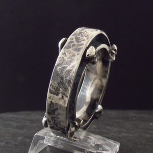May include: A silver ring with a textured band and a unique design featuring small spikes around the edge.