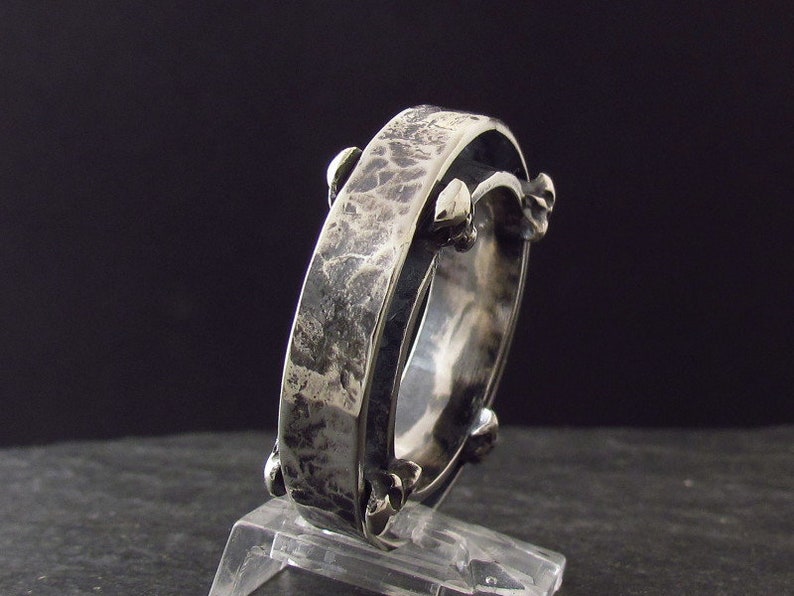 May include: A silver ring with a textured band and a unique design featuring small spikes around the edge.
