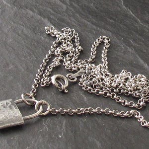 Op de afbeelding: Een zilveren ketting met een hangslotbedel. Het hangslot is gemaakt van getextureerd zilver en heeft een verweerde uitstraling.