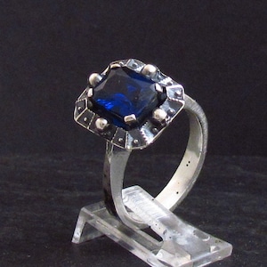 Puede incluir: Un anillo de plata con una gran piedra preciosa azul oscuro engastada en un diseño geométrico detallado.