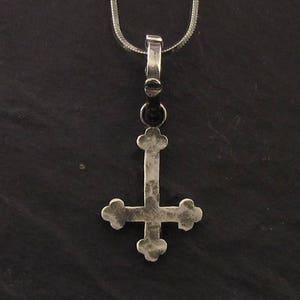 May include: A silver pendant in the shape of an upside-down cross. The pendant is on a silver chain.