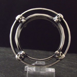 May include: A silver ring with four skull details around the band. The ring is double-banded and has a black enamel inlay.