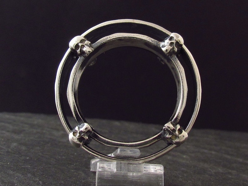 May include: A silver ring with four skull details around the band. The ring is double-banded and has a black enamel inlay.