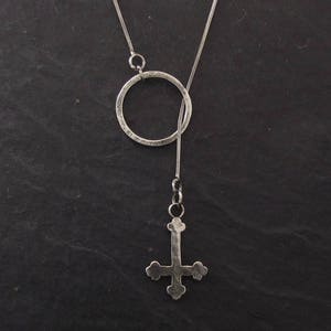 May include: A silver necklace with a circle pendant and a silver upside-down cross pendant.
