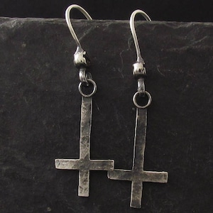 May include: A pair of silver upside-down cross earrings. The earrings are made of textured metal and have a simple, minimalist design.
