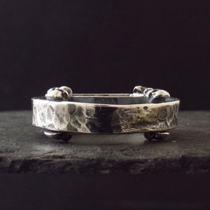 May include: A silver hammered metal ring with a textured surface and decorative accents. The ring is open and has a hinged design.