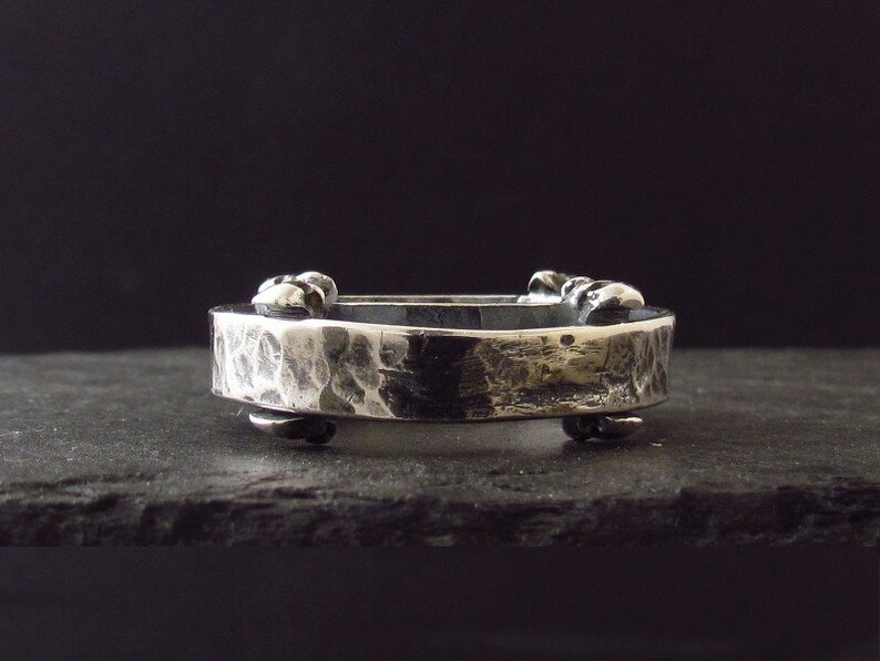 May include: A silver hammered metal ring with a textured surface and decorative accents. The ring is open and has a hinged design.