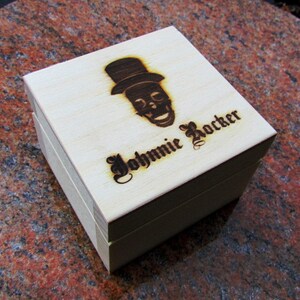 May include: A wooden box with a skull and top hat design and the text "Johnnie Rocker" engraved on the top.