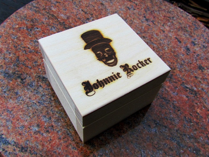 May include: A wooden box with a skull and top hat design and the text "Johnnie Rocker" engraved on the top.