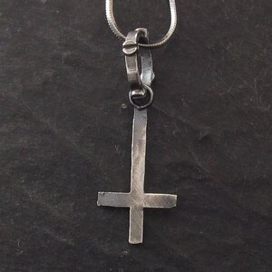 May include: A silver pendant necklace featuring a silver upside-down cross.