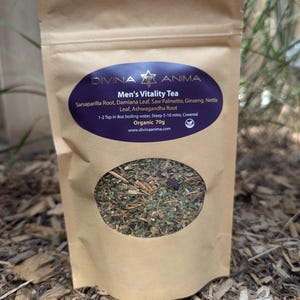 May include: A brown paper bag of Men's Vitality Tea with a clear oval window showing the tea blend. The label is purple with white text listing ingredients like Sarsaparilla Root and Ginseng. The bag is labeled "Organic 70g".