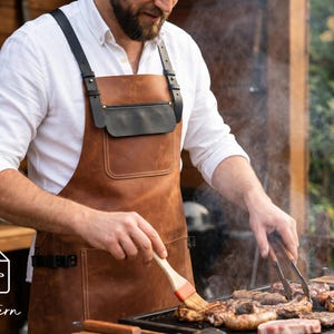 Könnte beinhalten: Eine Person trägt eine braune Lederschürze mit schwarzen Trägern und einer schwarzen Tasche beim Grillen von Fleisch. Die Person verwendet einen Pinsel, um das Fleisch auf dem Grill zu bestreichen. Die Schürze ist ein PDF-Muster.