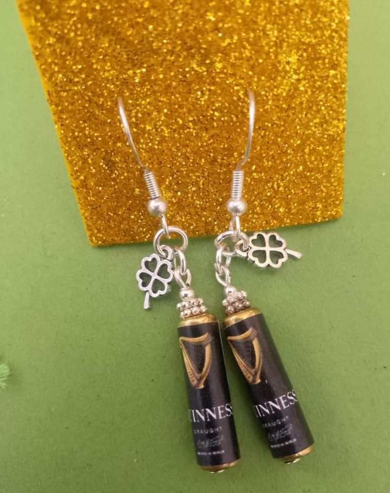 May include: A pair of silver earrings with a black and gold Guinness can charm and a silver shamrock charm.