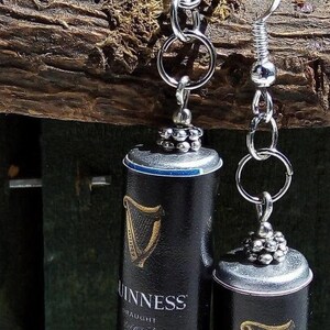 May include: A pair of silver dangle earrings featuring miniature black Guinness cans with the iconic harp logo and the text "Guinness Draught Brewed in Dublin".
