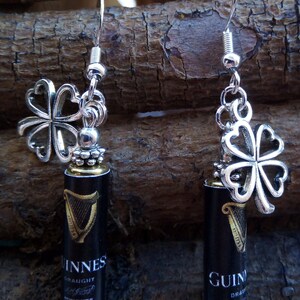 May include: Silver earrings with a shamrock charm and a miniature Guinness beer bottle charm. The bottle charm has the words "Guinness Draught" printed on it.
