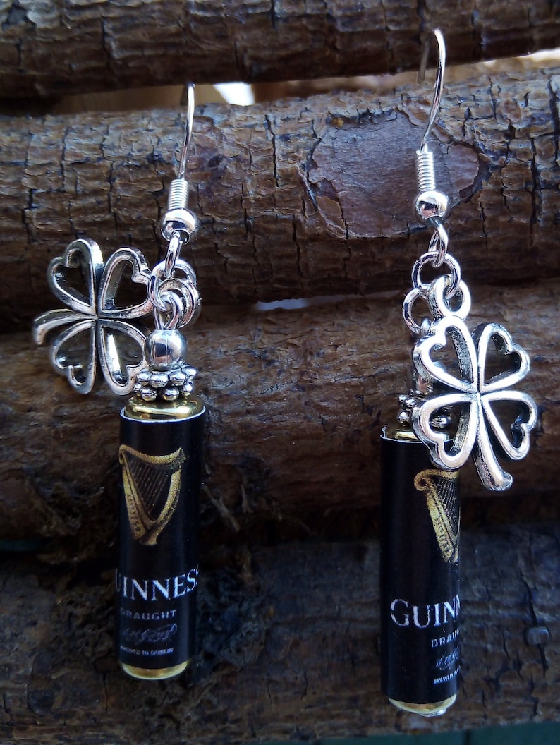May include: Silver earrings with a shamrock charm and a miniature Guinness beer bottle charm. The bottle charm has the words "Guinness Draught" printed on it.