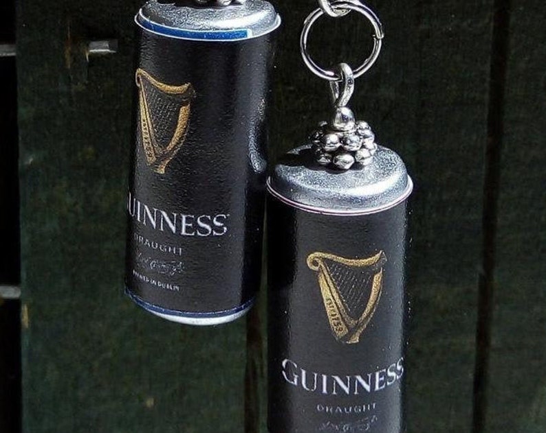 May include: Two black and gold Guinness beer can charms. The charms are made from recycled beer cans and have a silver chain attached.