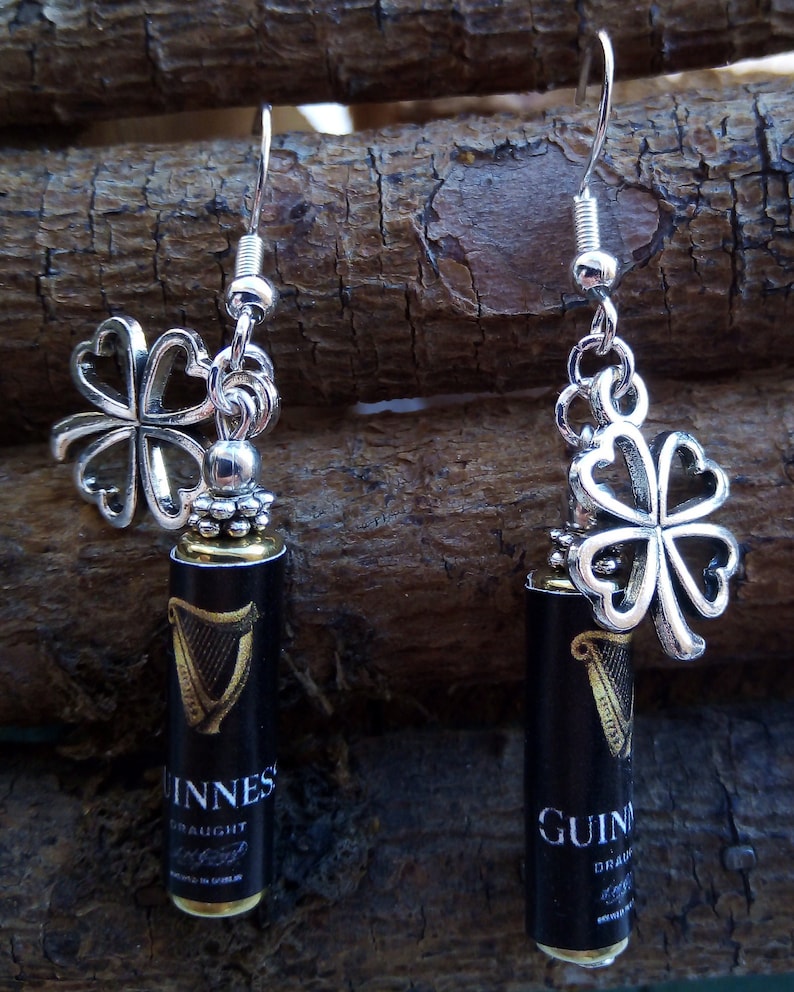May include: A pair of silver earrings with a shamrock charm and a miniature Guinness beer bottle charm. The bottle charm is black with gold lettering that reads "Guinness Draught".